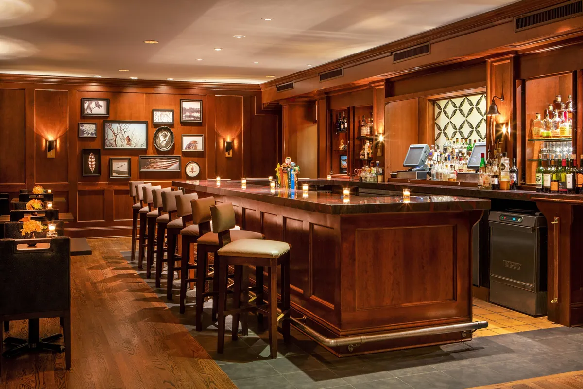 This interior image showcases a sophisticated bar area, with a stylish counter, an array of bottles on display, and framed pictures enhancing the inviting ambiance. The scene suggests guests socializing, unwinding with drinks, and enjoying themed evenings or live music after a day of outdoor activities.