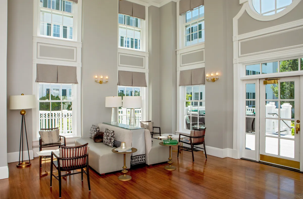 This image depicts a bright, inviting guest room with large windows that allow abundant natural light to fill the space. Modern furniture, including a seating area with a stylish coffee table, and decorative wall sconces create a sophisticated yet welcoming atmosphere. The decor subtly hints at regional heritage while maintaining a contemporary feel. The windows potentially offer views of the Green Mountains, contributing to a tranquil ambiance.